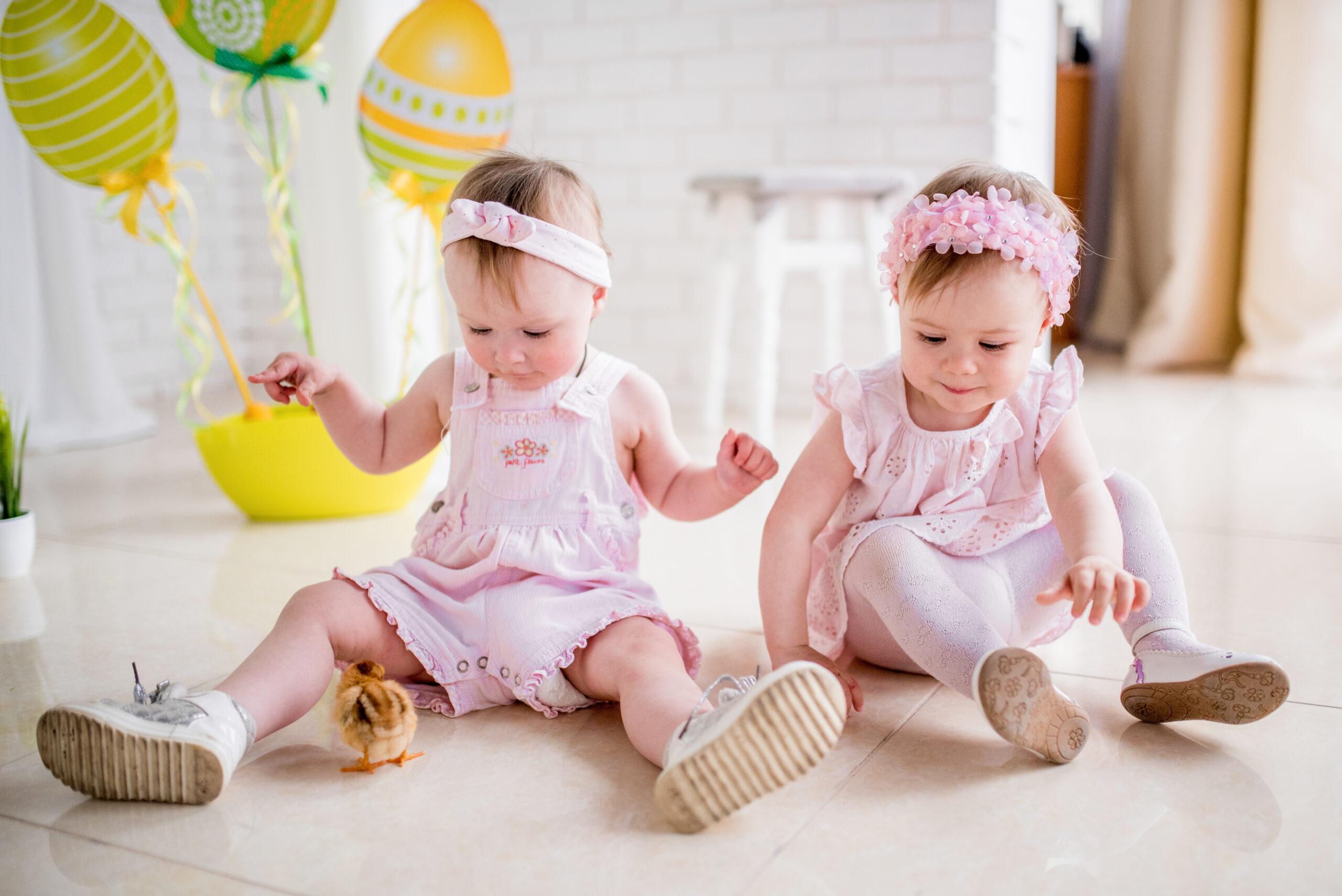 Two little girls in pink dresses play on the floor in the studio with Easter decor